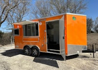 an orange food trailer parked in a dirt lot